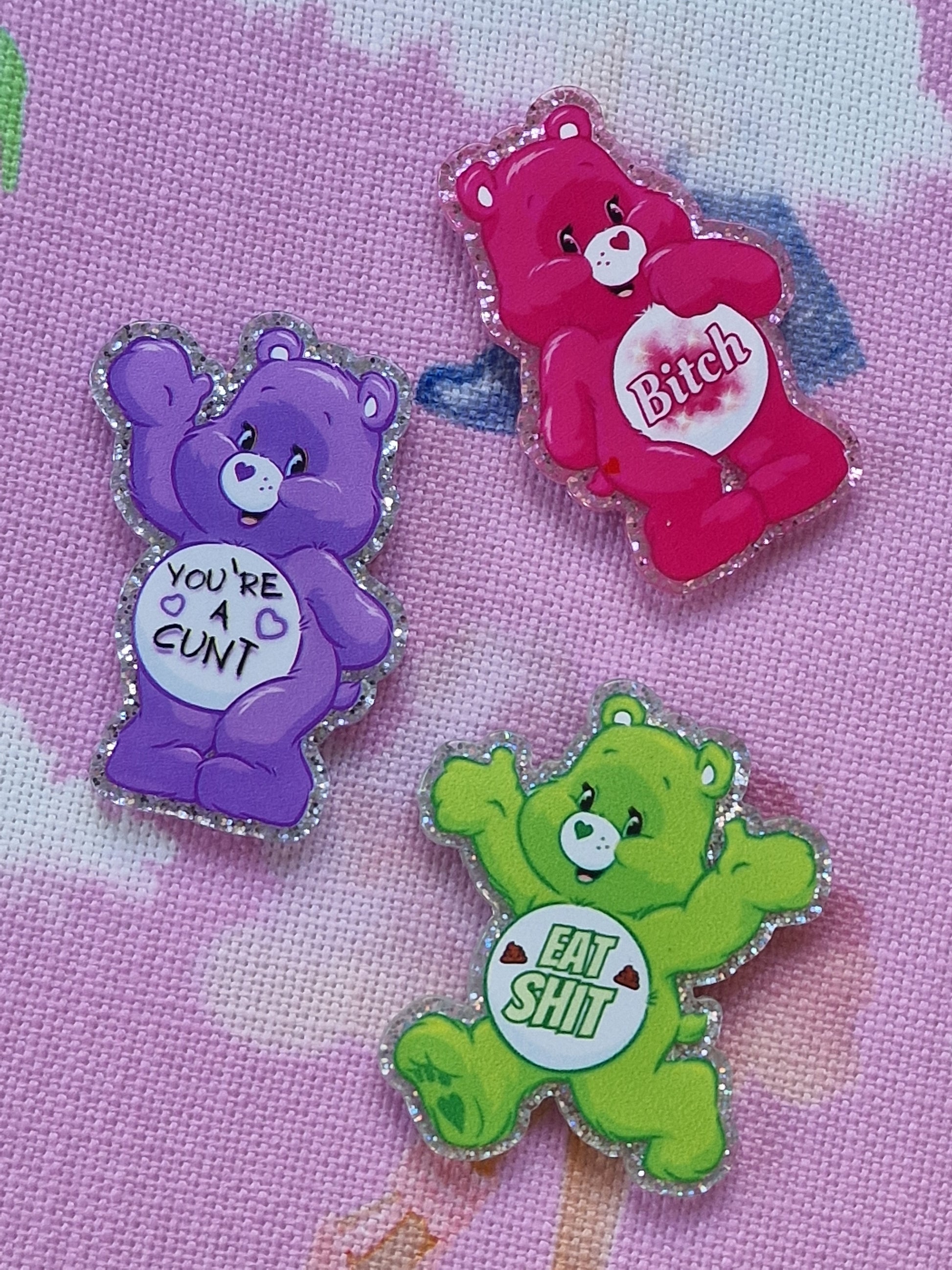 Three colorful swear bear pins with offensive text on a pink background